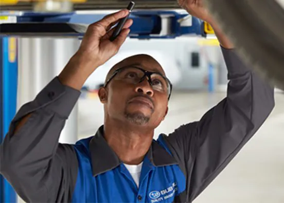 A Subaru technician under a Subaru vehicle 'Schedule Service'